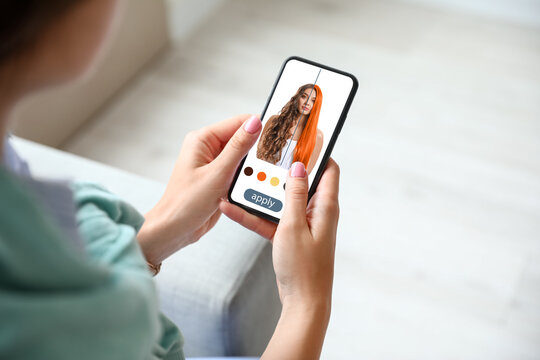 Young woman with modern mobile phone using hair style application at home