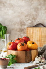 Wooden bowl of fresh colorful tomatoes, garlic, basil and ingredients on textured background. Kitchen still life in rustic style. Copy space