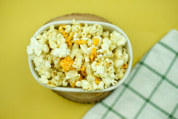 Popcorn in a white bowl on yellow background, top view