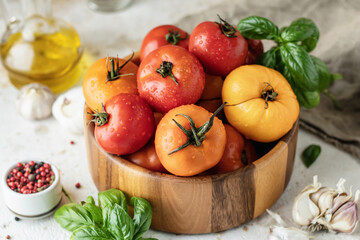 Wooden bowl of fresh colorful tomatoes, garlic, basil, pepper and olive oil on textured background. Kitchen still life in rustic style