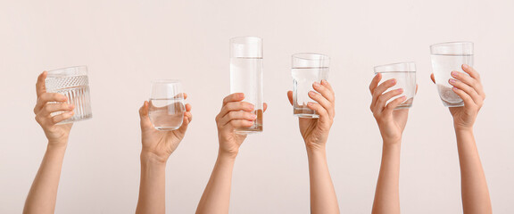 Female hands with glasses of water on light background