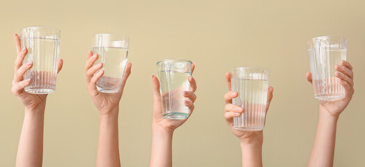 Female hands with glasses of water on beige background