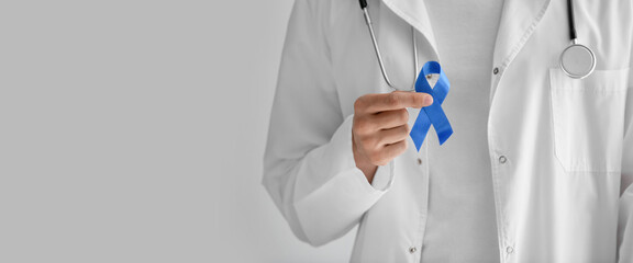 Doctor holding blue ribbon on light background with space for text, closeup. Prostate cancer awareness concept
