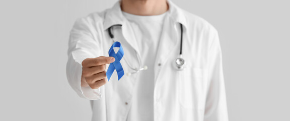 Doctor holding blue ribbon on light background, closeup. Prostate cancer awareness concept