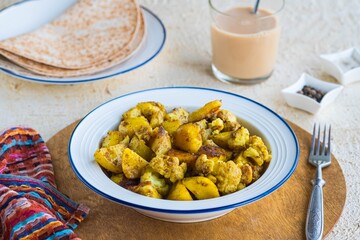 Cauliflower with potatoes and spices in a white plate on a light concrete background. Indian food. Vegan food.