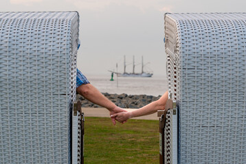 Older couple holding hands while sitting in beach chairs in Cuxhaven, Germany.