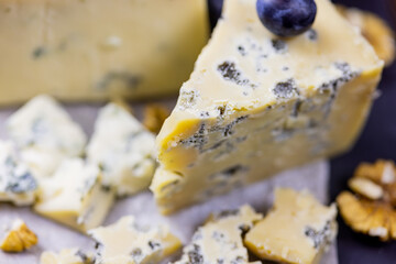 Tasty blue cheese served with grape and green on a wooden background. Dorblu cheese pieces