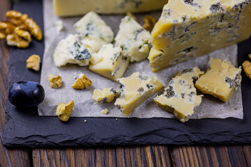 Tasty blue cheese served with grape and green on a wooden background. Dorblu cheese pieces