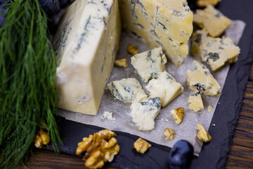 Tasty blue cheese served with grape and green on a wooden background. Dorblu cheese pieces