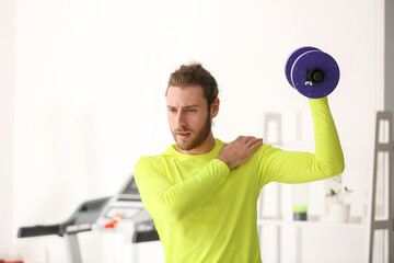 Sporty young man using dumbbells in gym