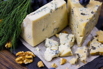 Tasty blue cheese served with grape and green on a wooden background. Dorblu cheese pieces