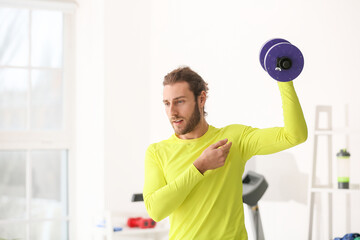 Sporty young man using dumbbells in gym