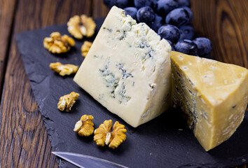 Tasty blue cheese served with grape and green on a wooden background. Dorblu cheese pieces