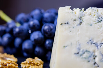 Tasty blue cheese served with grape and green on a wooden background. Dorblu cheese pieces