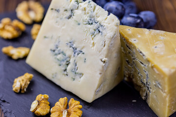 Tasty blue cheese served with grape and green on a wooden background. Dorblu cheese pieces