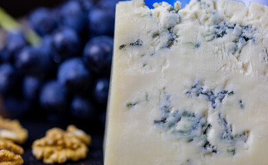 Tasty blue cheese served with grape and green on a wooden background. Dorblu cheese pieces