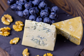 Tasty blue cheese served with grape and green on a wooden background. Dorblu cheese pieces