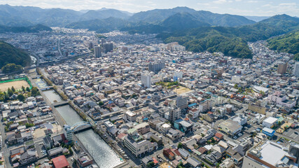 Fototapeta premium 空撮 鳥瞰 ドローン 地方都市 街並み 風景 都市景観 市街地 住宅街 建物 川 橋 道路 山 青空 京都 舞鶴 西舞鶴 日本 | Aerial Drone View of West Maizuru Cityscape Residential Area River and Mountains Kyoto Japan