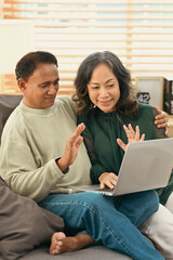 Obraz premium Happy retired couple making video call with family or friends on laptop while spending time together at home