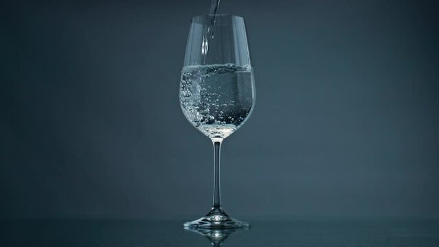 Pure water filling glass at dark background closeup. Bubbles rising transparent