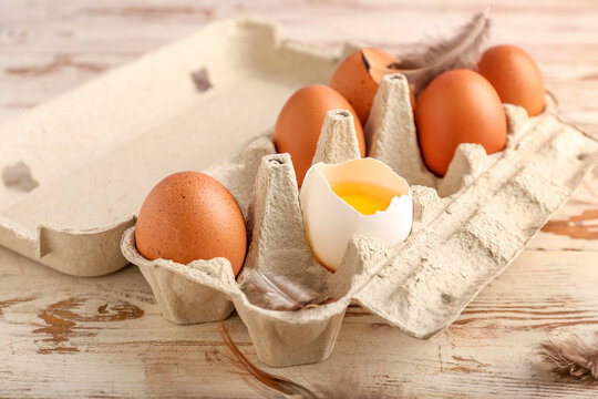 Cardboard holder with chicken eggs on light wooden background, closeup