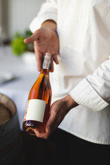 A sommelier offers a bottle of wine to a restaurant visitor. Hands of a waiter with a bottle of rose wine close-up
