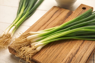 Board with bunch of fresh green onion on light wooden background, closeup