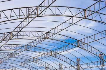 Curve lines pattern of metal roof beam structure of large dome event tent against clouds on blue sky background