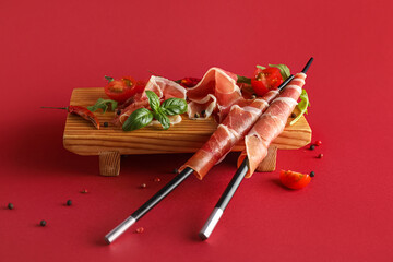 Wooden board with slices of delicious jamon, spices and tomatoes on color background