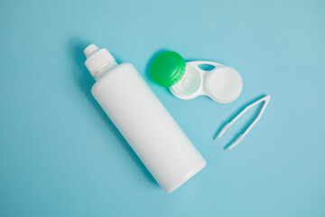 Packages with contact lenses, case, tweezers and drops on blue background