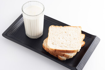A Glass of milk and whole wheat sliced bread on a black tray or plate for food and healthy concept with copy space for text isolated on white background