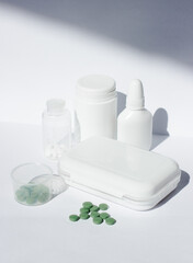 A small first aid kit with pills and a cross on the lid. There are jars of medicines nearby. All this on a white background