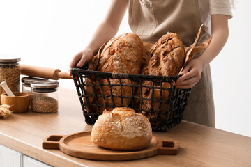 Young woman holding basket with loaves of fresh bread on light background