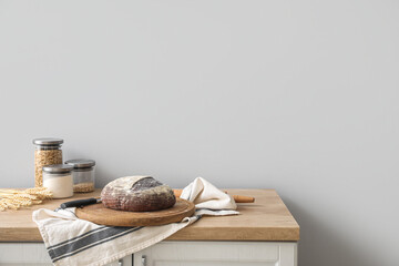 Board with fresh bread on kitchen counter near grey wall