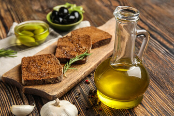 Decanter with fresh olive oil and bread on wooden table, closeup