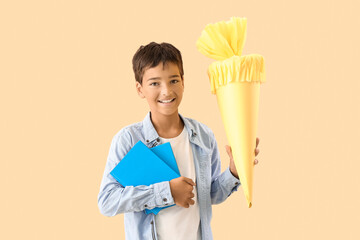 Little boy with yellow school cone and books on beige background