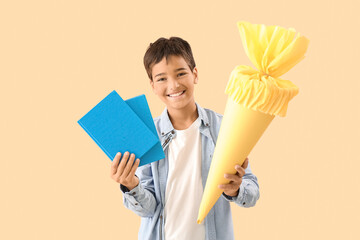 Little boy with yellow school cone and books on beige background