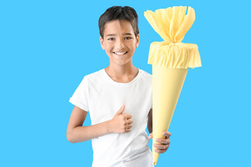 Little boy with yellow school cone showing thumb-up on blue background
