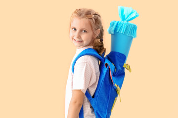 Cute little girl with school cone and backpack on beige background