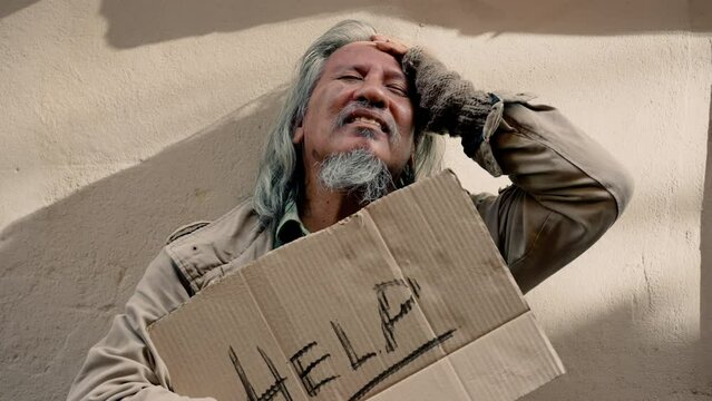 4K, Portrait of a homeless Asian man standing holding a sign for help in hopes but not being rescued until he is helpless, stressed because he has no home to live and has no work to eat for days.
