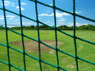 バックネット越しに見る夏の江戸川河川敷の野球場風景