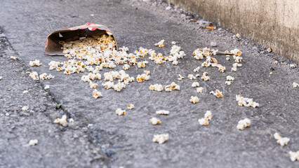 Popcorn in a cardboard box lies on concrete ground outside. The man dropped the popcorn and didn't clean it up by littering the environment.