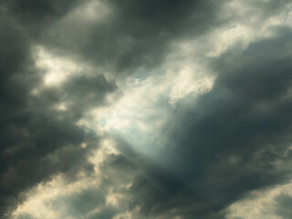 Pokryte szarymi chmurami niebo. Między chmurami znajdują się przerwy przez które można dostrzec błękit nieba i przedzierają się smugi światła.
