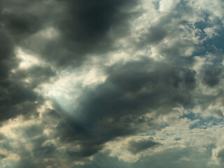 Pokryte szarymi chmurami niebo. Między chmurami znajdują się przerwy przez które można dostrzec błękit nieba i przedzierają się smugi światła. - obrazy, fototapety, plakaty
