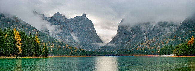 Panoramic over the Toblacher Lake Lago di Dobbiaco and Dolomite mountain summits nearby in Autumn October colors at foggy morning, Dolomites, South Tyrol, Italy. © neurobite