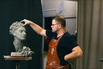 Man sculptor creates sculpt bust clay human woman sculpture. Statue craft creation workshop. Small business.