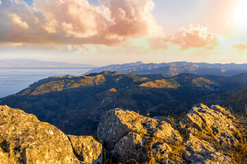 Obraz premium amazing mountain landscape of beautiful cloudy sunset above rocks , blue sea and isles with a rock on foreground
