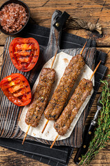 Roasted Turkish Adana shish kebab on a board with grilled tomato. Wooden background. top view