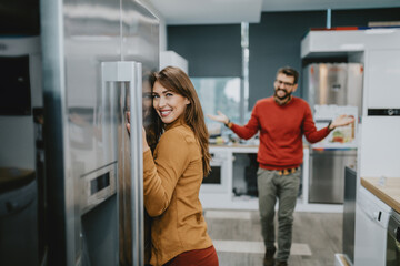 Beautiful happy young couple, satisfied customers choosing fridges in appliances store.