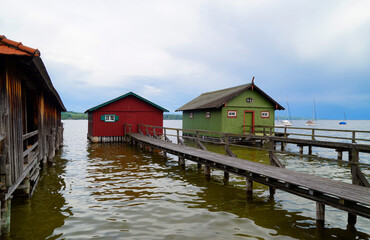a long wooden pier leading to the colorful boat houses on lake Ammersee with sailing boats and the...